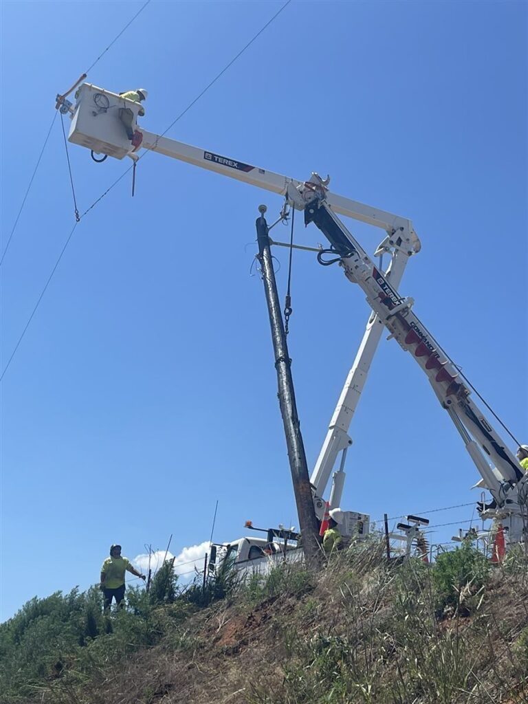Bucket truck working on a pole along a grassy hillside
